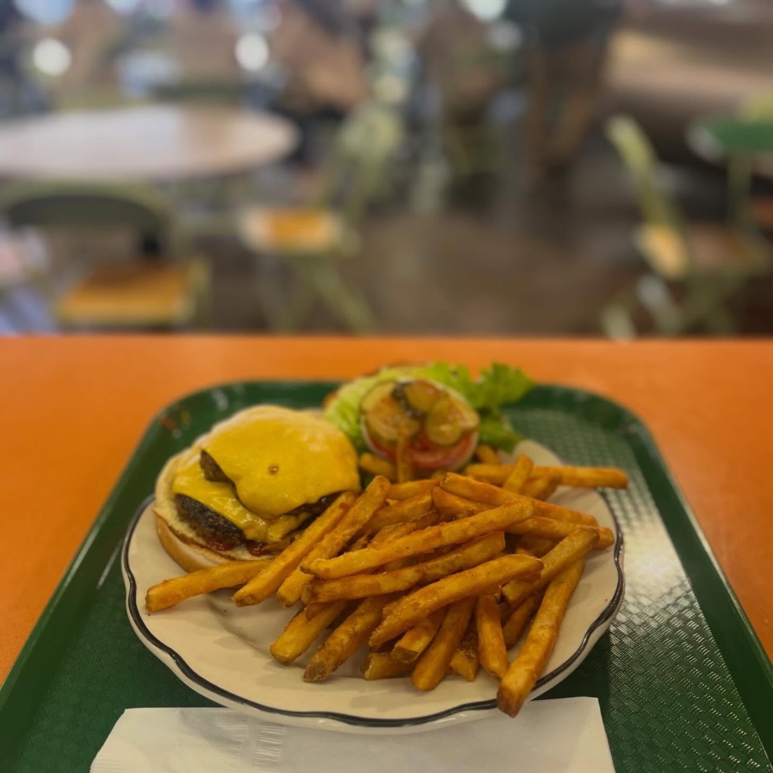 A double cheeseburger with a pile of fries on a green tray.